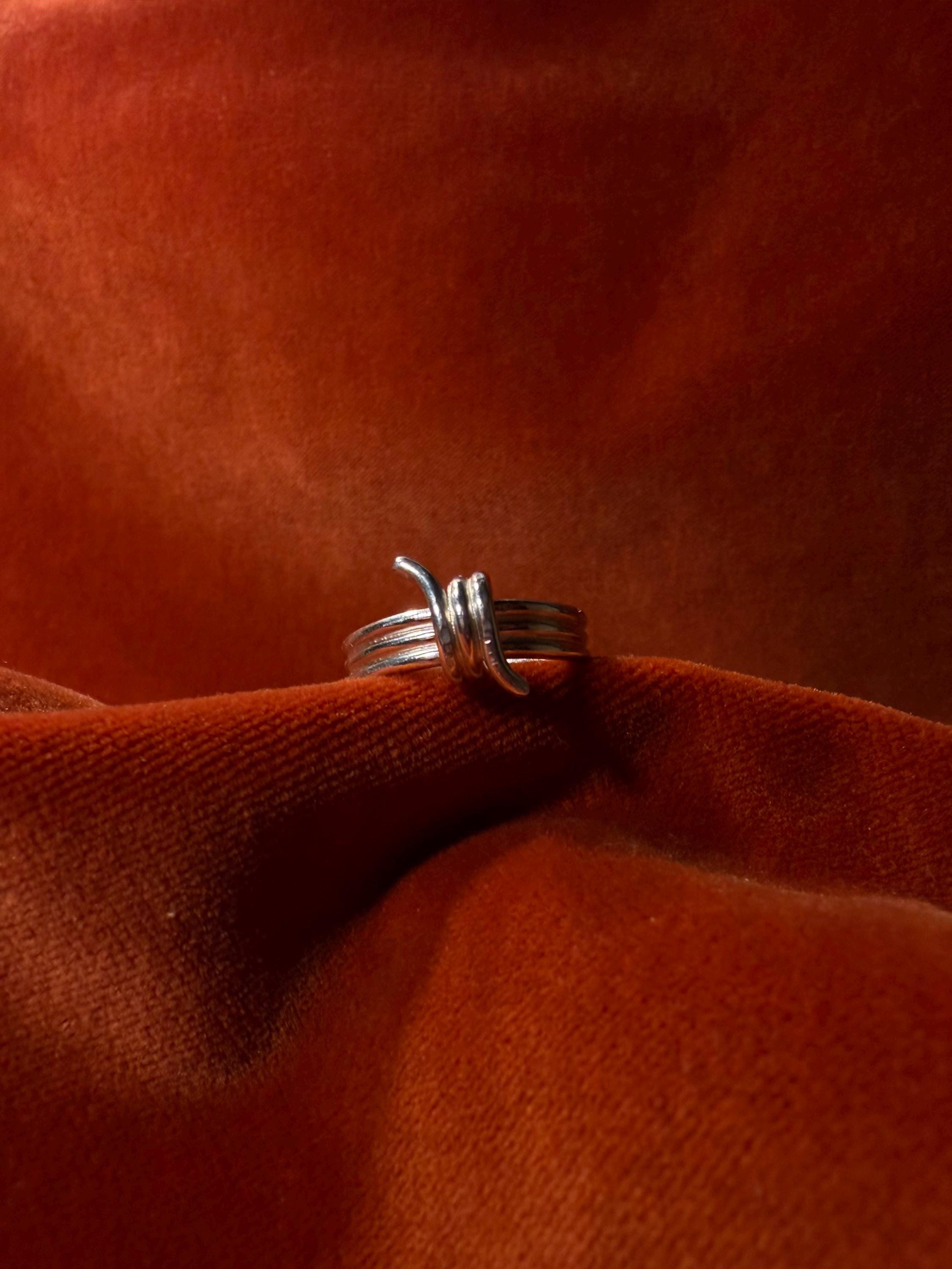 Silver ring featuring a barbed wire design. Staged on an orange velvet background.