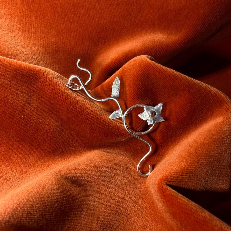 Silver jasmine flower vine charm laying against an orange velvet background.