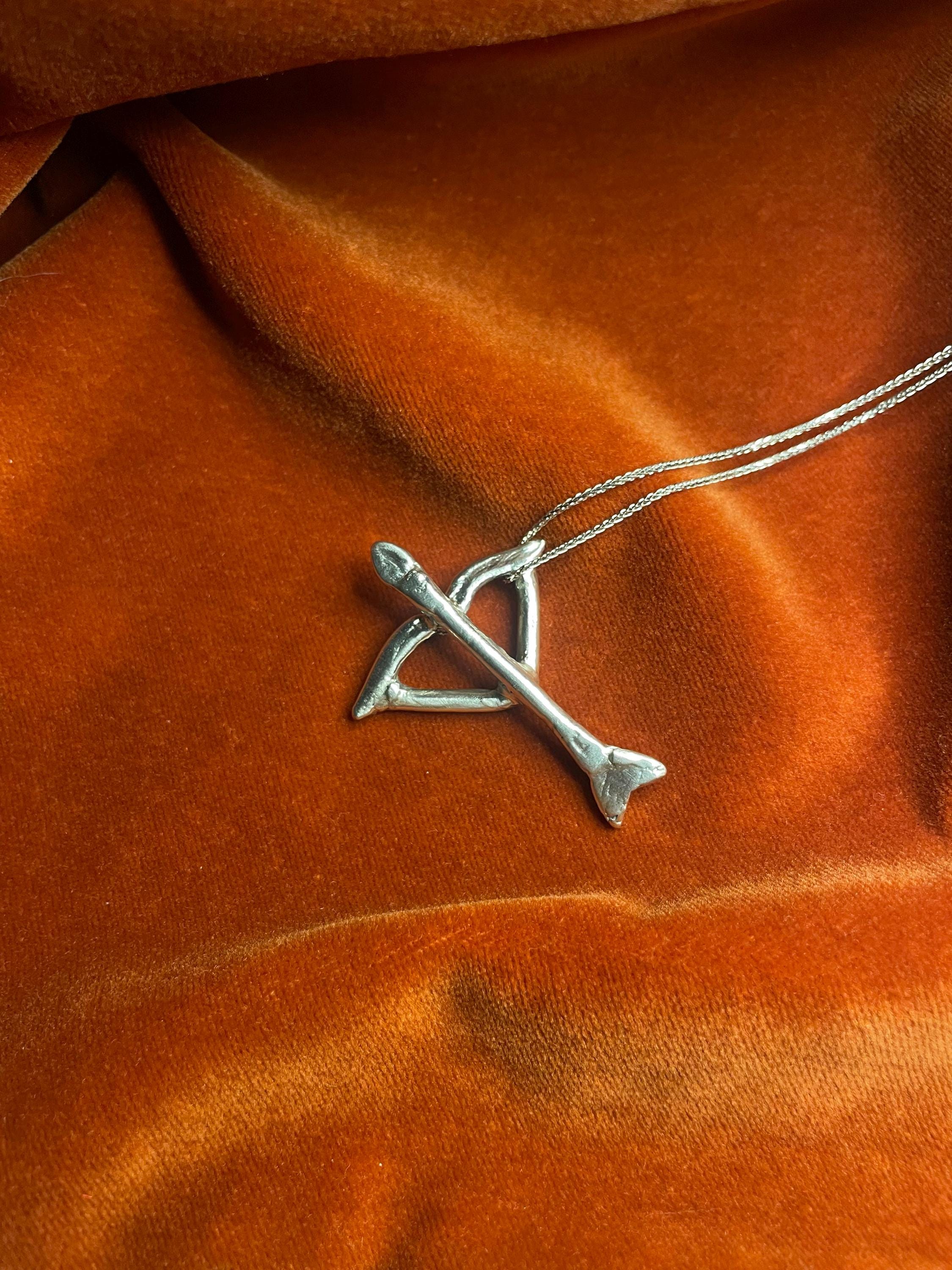 Silver bow and arrow charm on a silver chain. Laying against an orange velvet background.