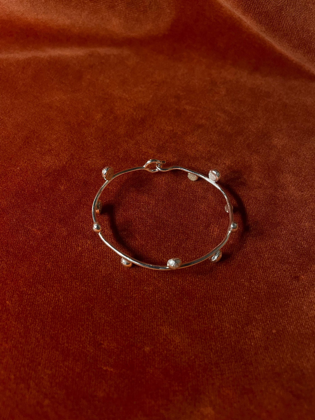 Top down visual of a silver bracelet with ten small orbs along the bracelet. Staged on an orange velvet backdrop.