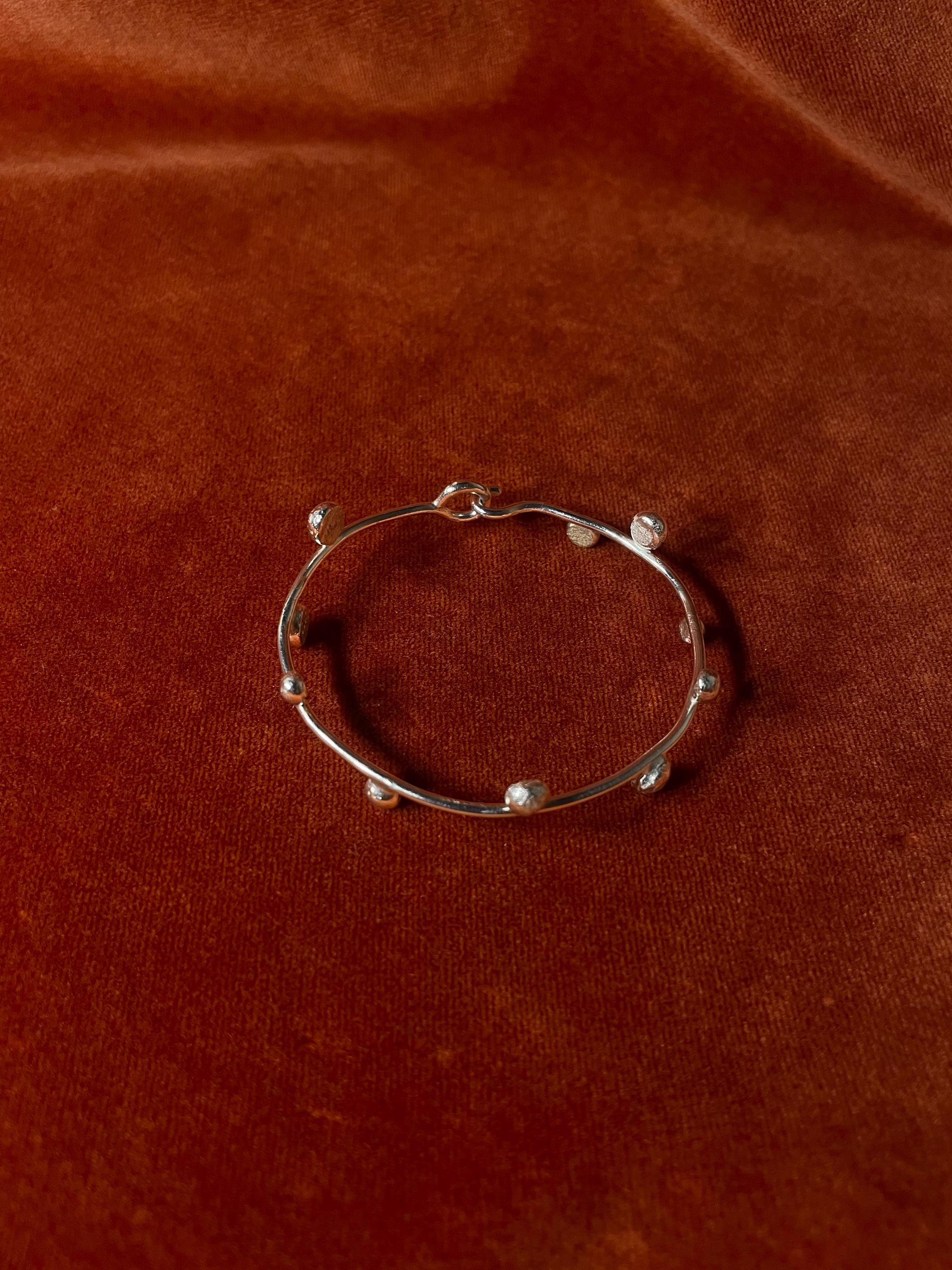 Top down visual of a silver bracelet with ten small orbs along the bracelet. Staged on an orange velvet backdrop.