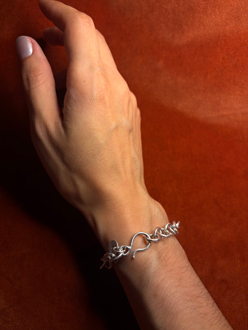 Model's arm, wearing a sterling silver chunky chain on their wrist with a hook clasp. Displayed on an orange velvet backdrop.
