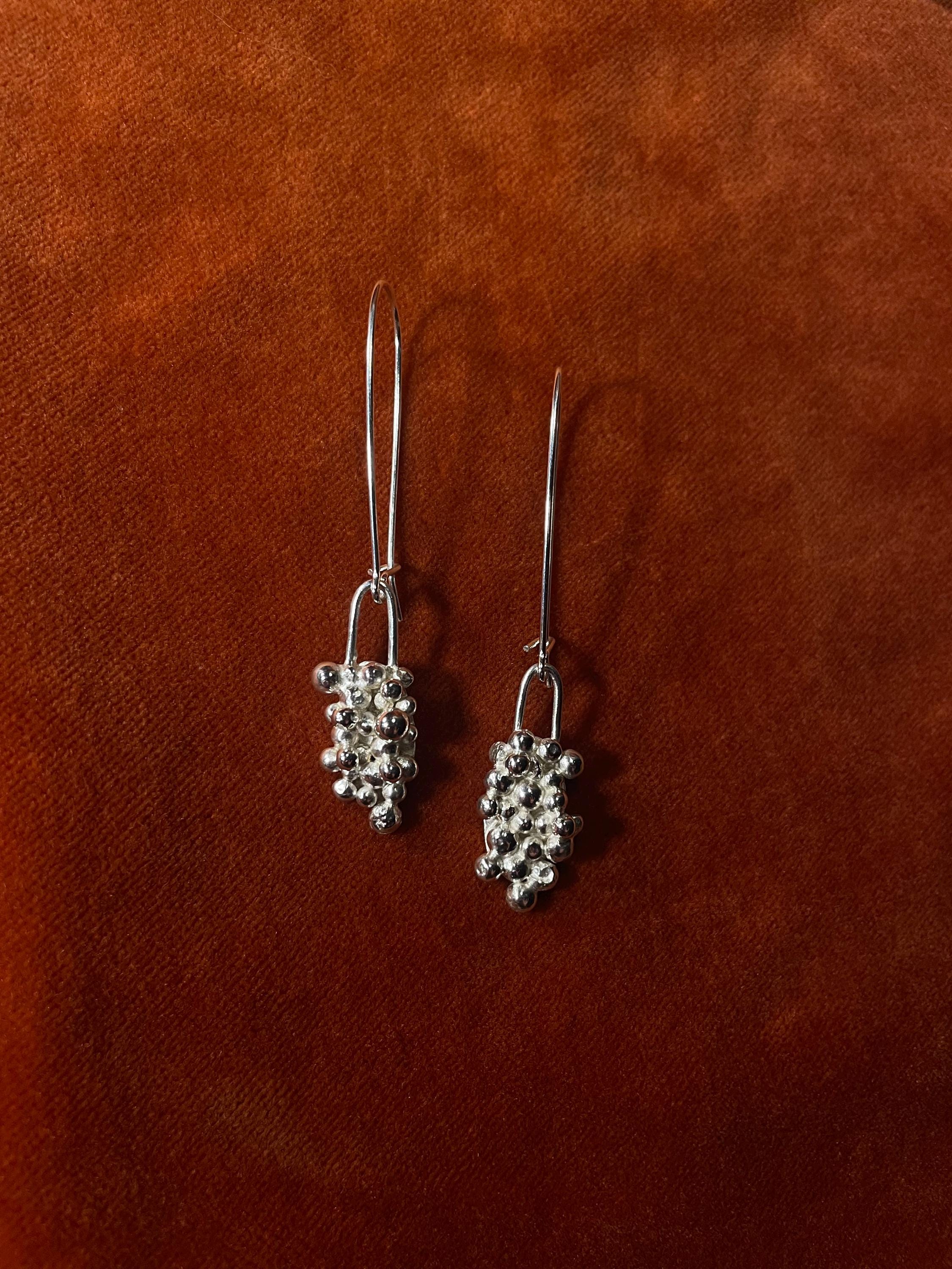 A pair of silver earrings with clusters of bubbles with an elongated clasp hook for a dangling style.