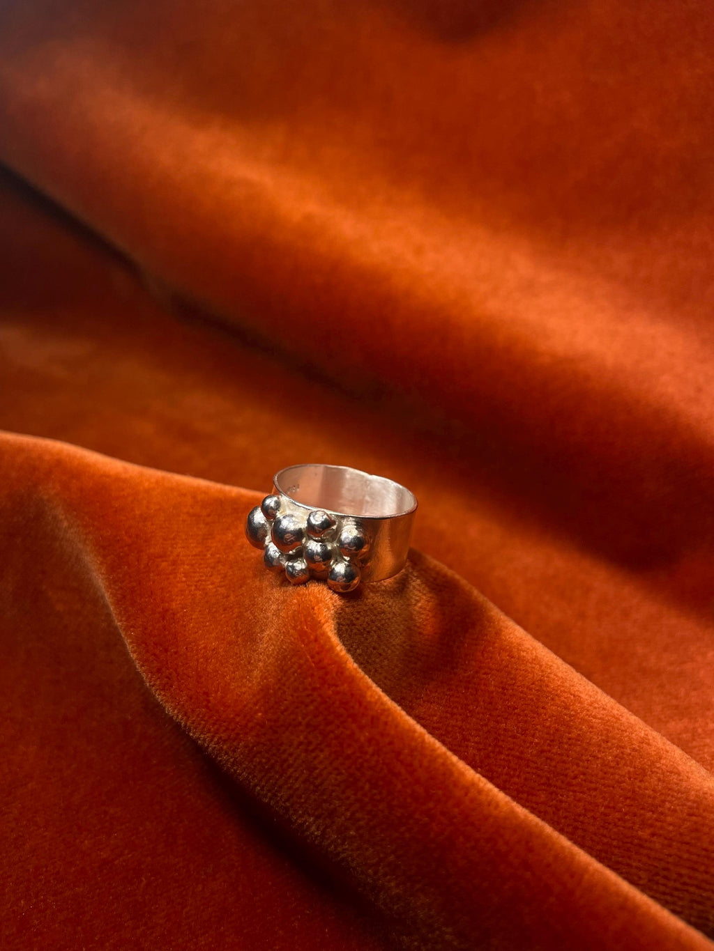 Silver ring with bubbles forming around the band laying on an orange velvet backdrop.