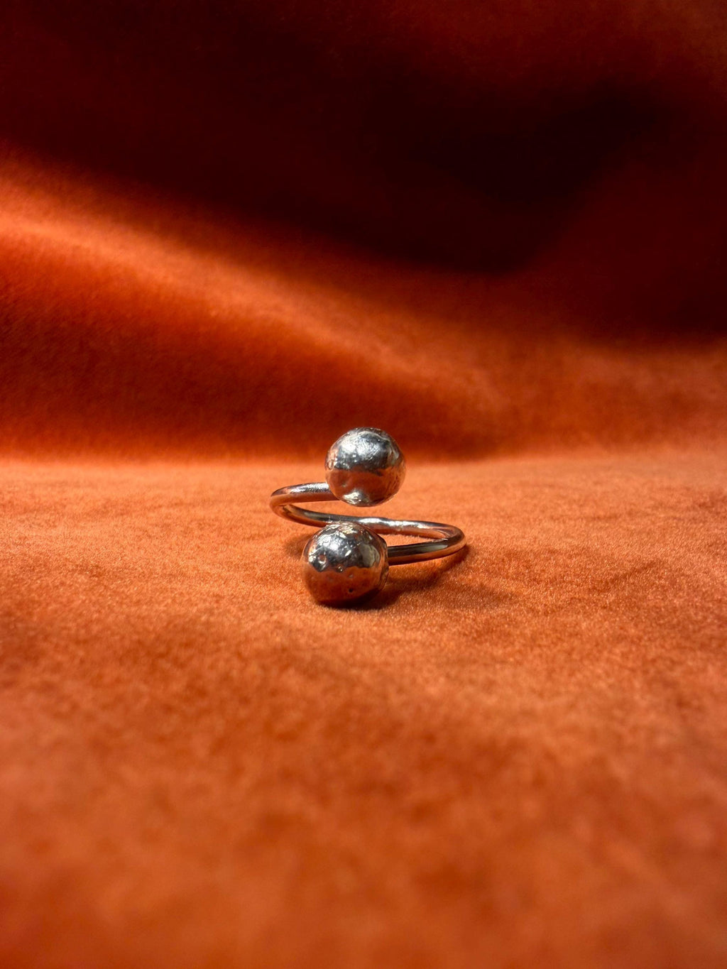 Silver ring with two orbs laying on an orange velvet backdrop.