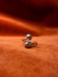 Silver ring with two orbs laying on an orange velvet backdrop.