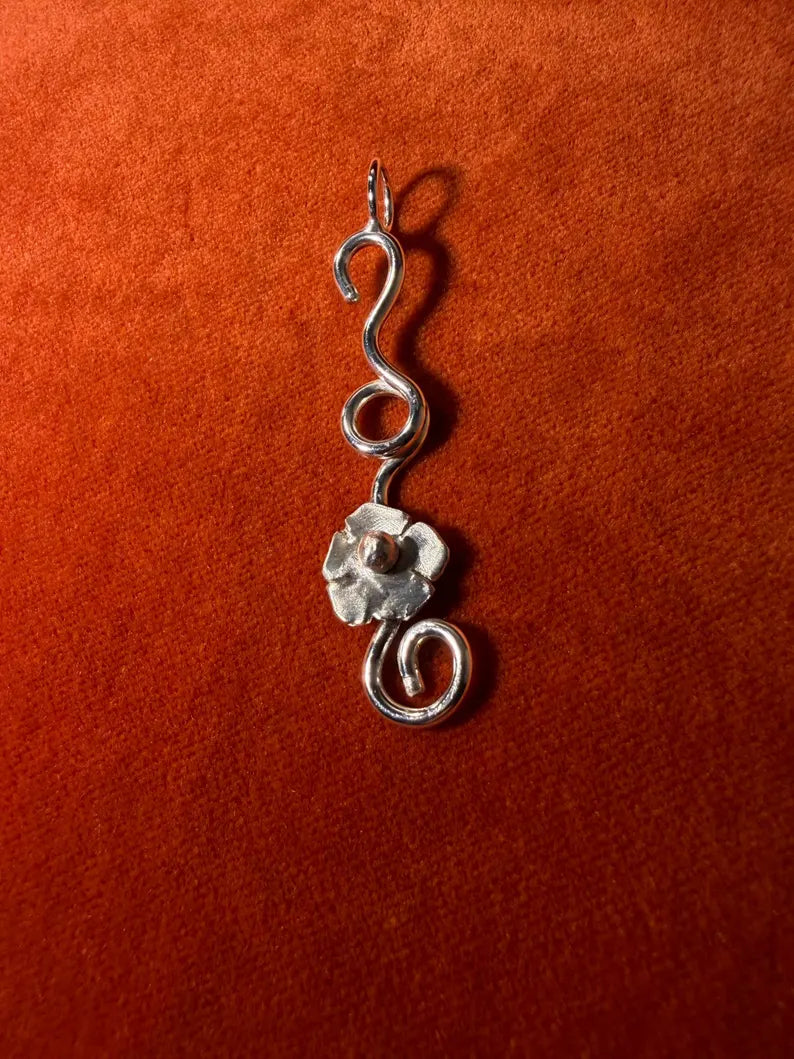 Silver flower vine charm laying against an orange velvet background.