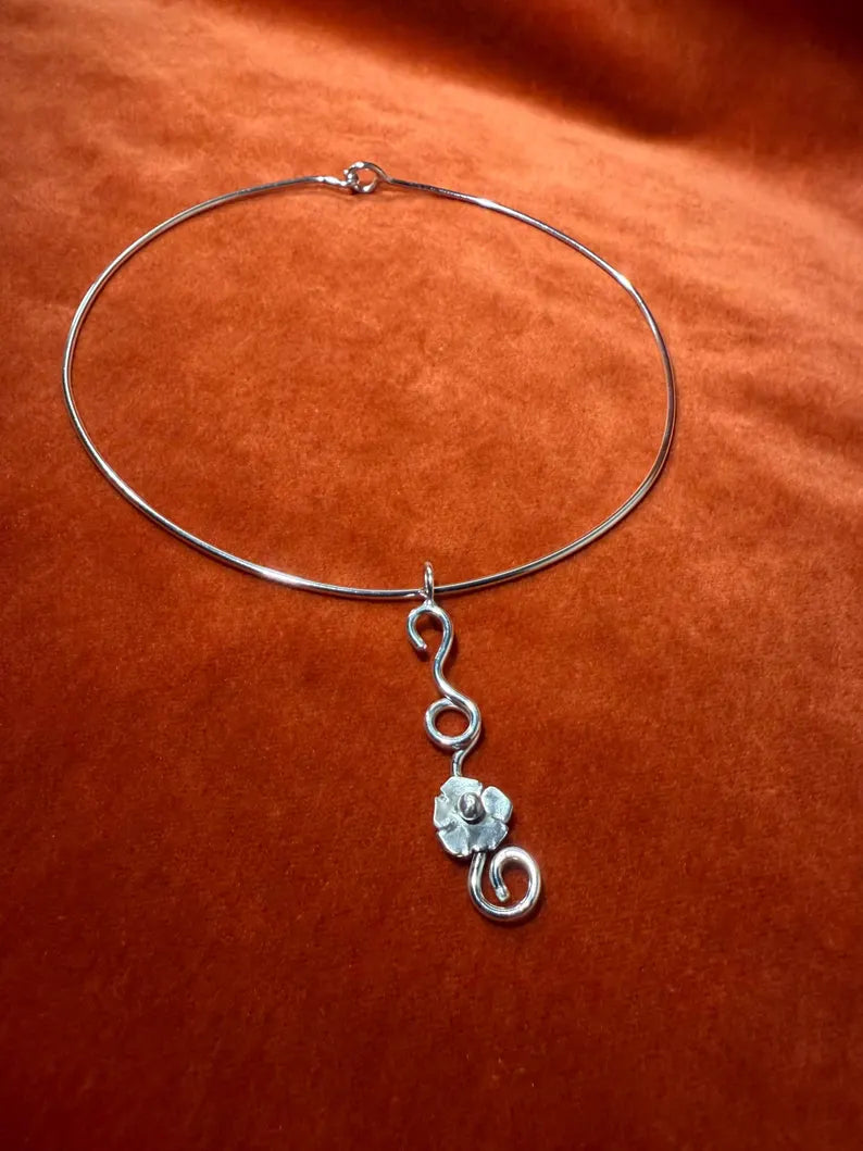 Silver choker with a silver flower vine charm laying against an orange velvet background.