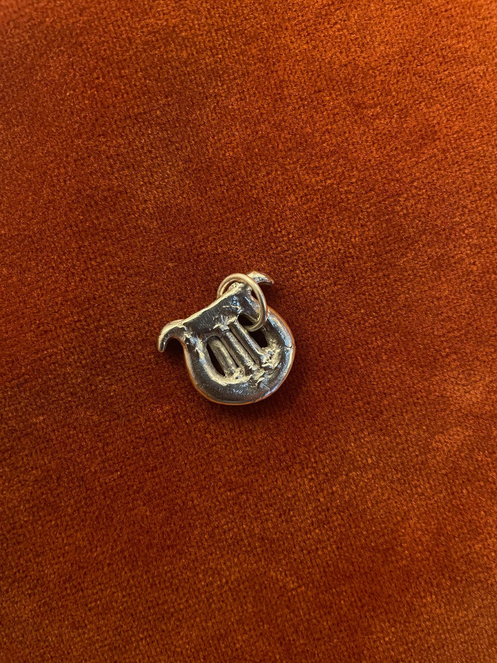 Silver harp with a silver jump ring. Staged against an orange velvet background.