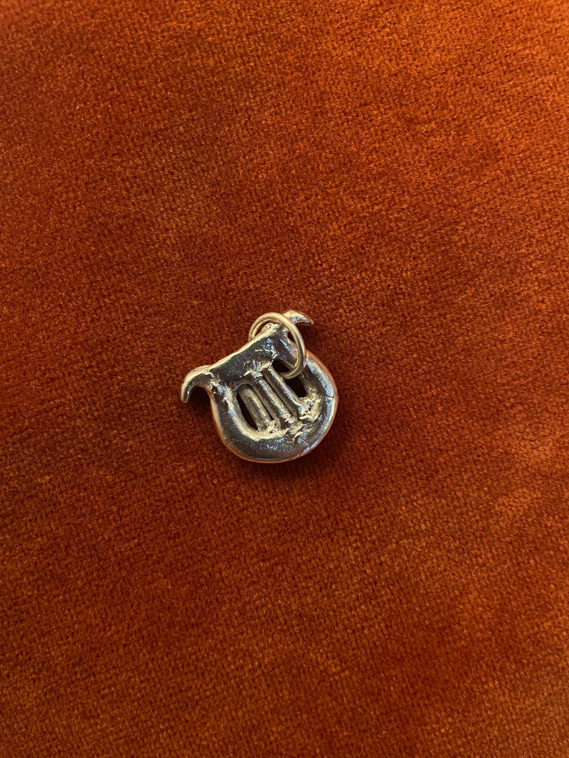 Silver harp with a silver jump ring. Staged against an orange velvet background.