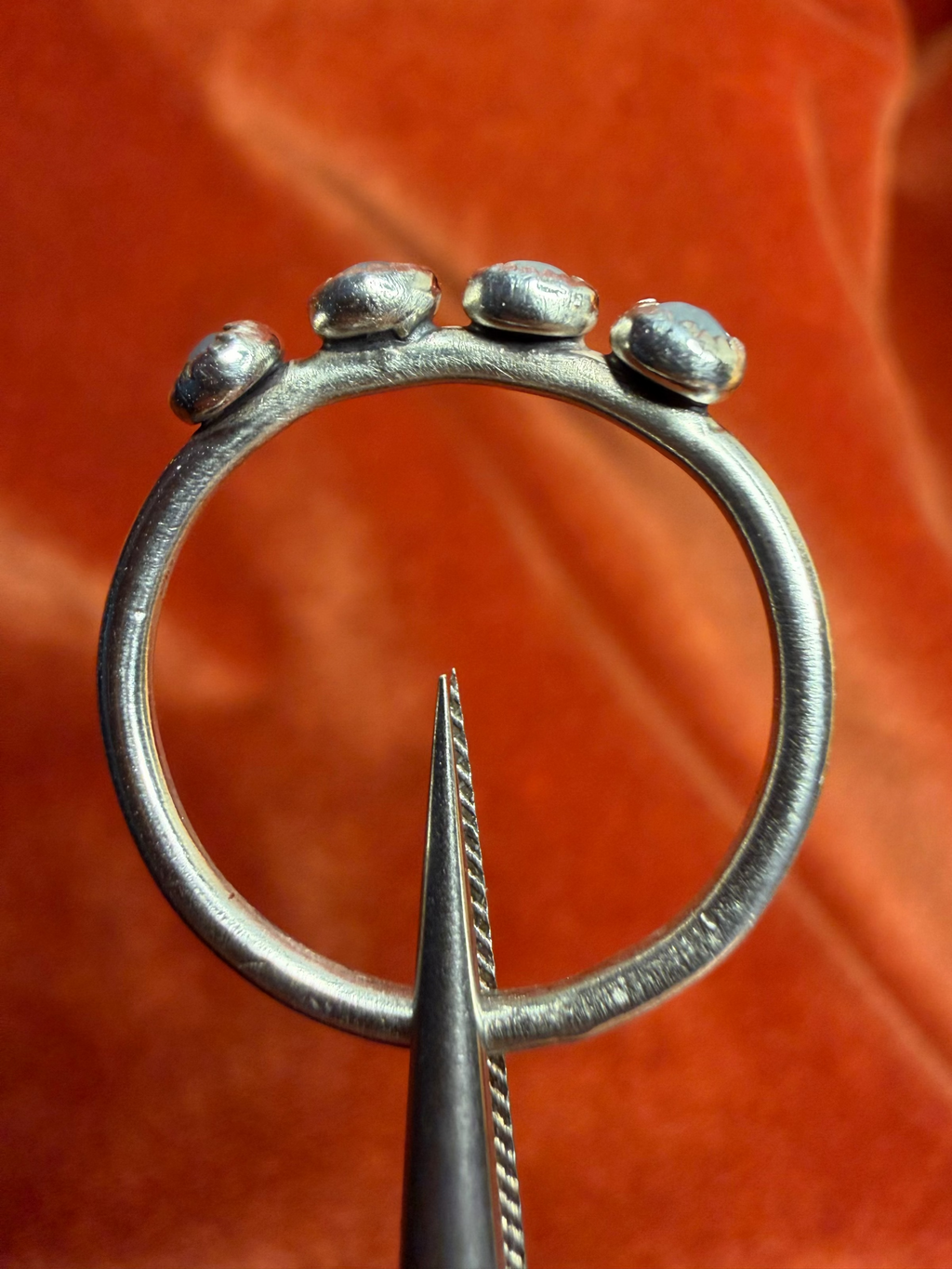Close up image of a silver ring with four small milky blue aquamarine stones, set in serrated bezels. Laid on a small thing band. Ring is held be silver tweezers.