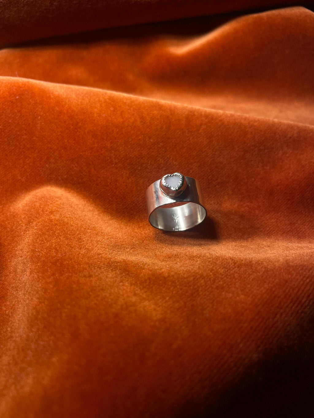 Silver ring with a pink opal stone set on a chunky band. Staged on an orange velvet backdrop.