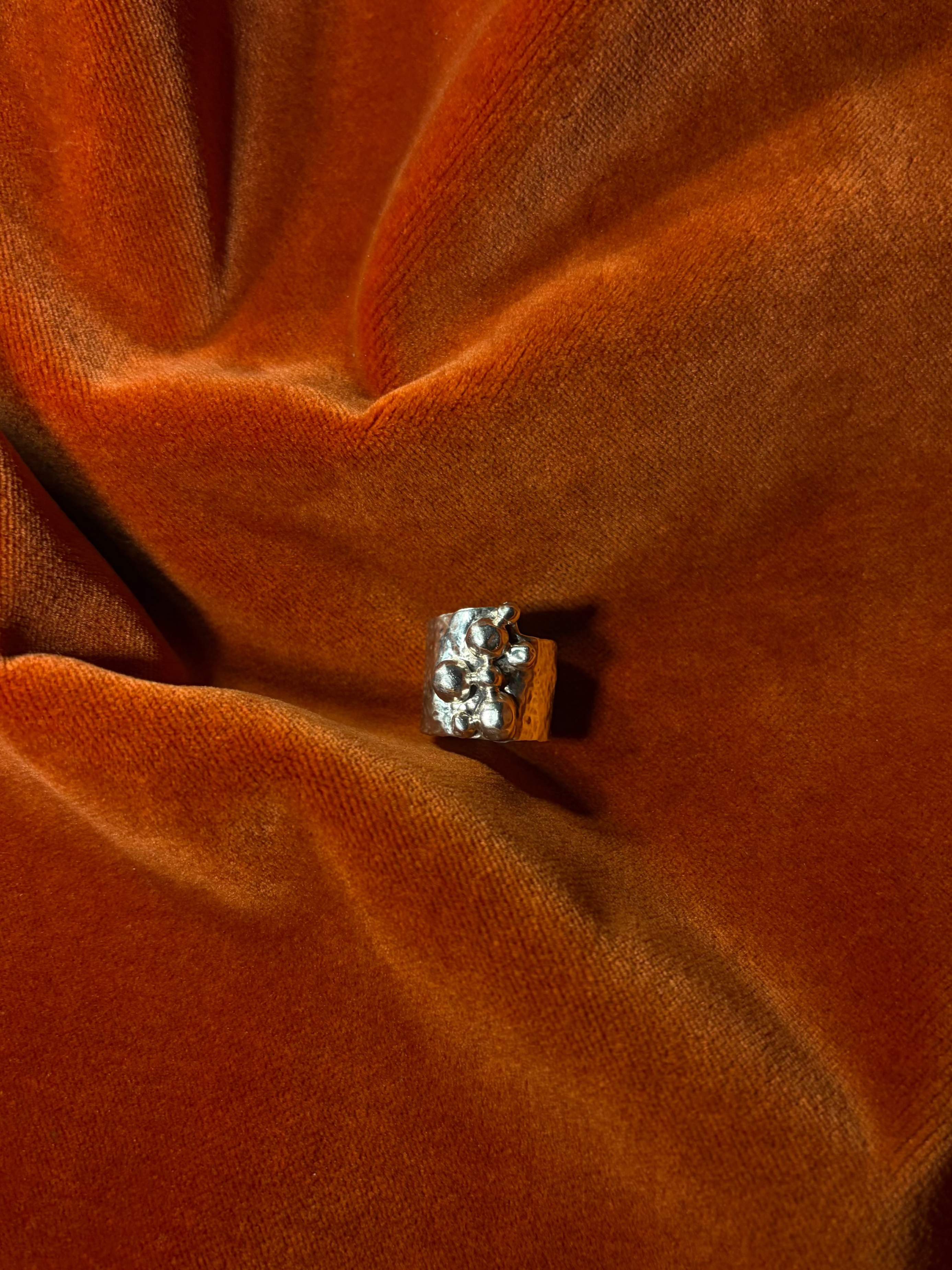 Close up image of a silver ring with a chunky hammered texture band. Seven varying sizes of orbs sit asymmetrically on top of the band.