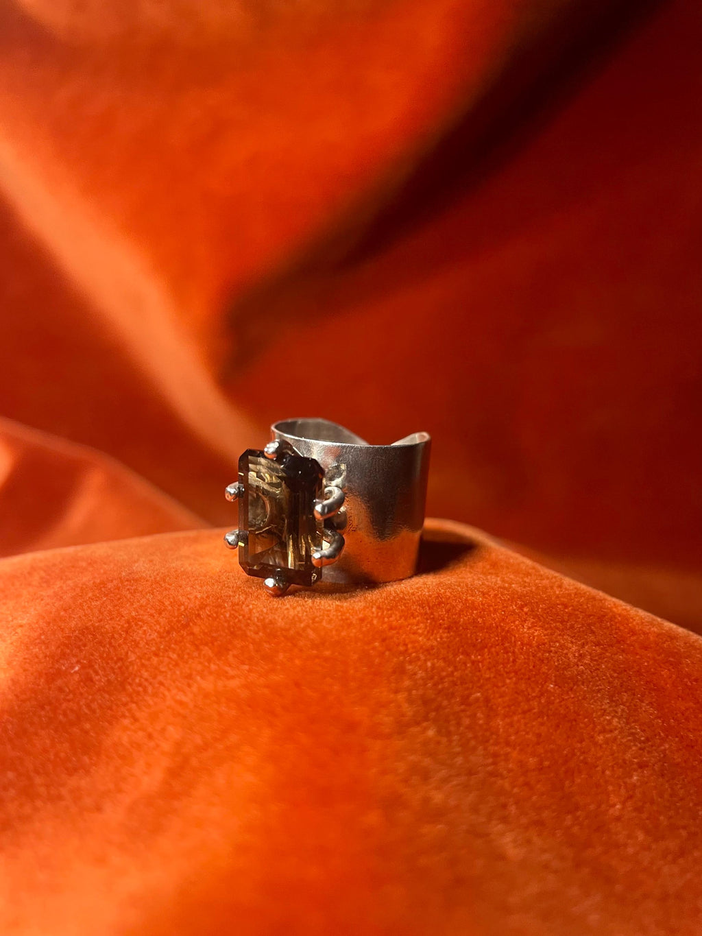 Silver ring with a smoky quartz emerald cut stone, set within five prongs on top of the large band. 