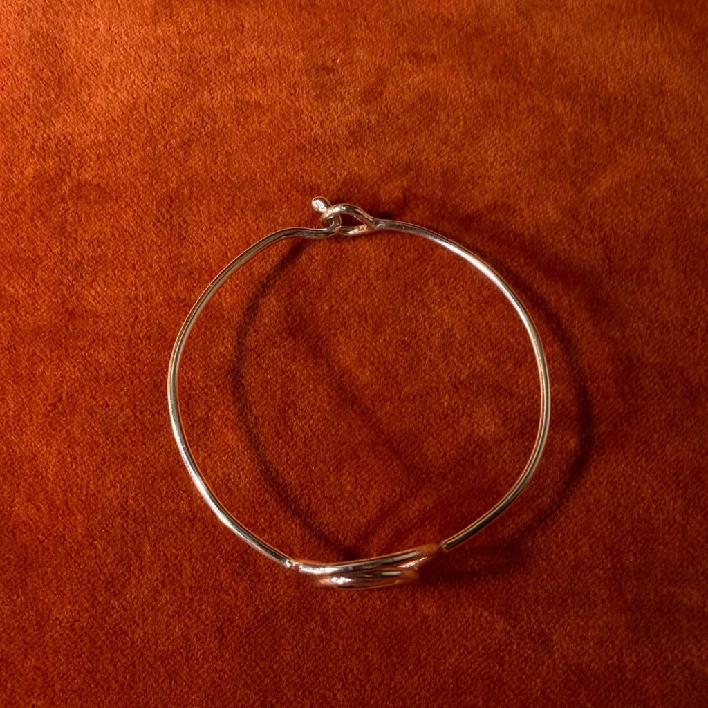 Silver bracelet with a spiral shape and a hook clasp. Pictured on a velvet backdrop.