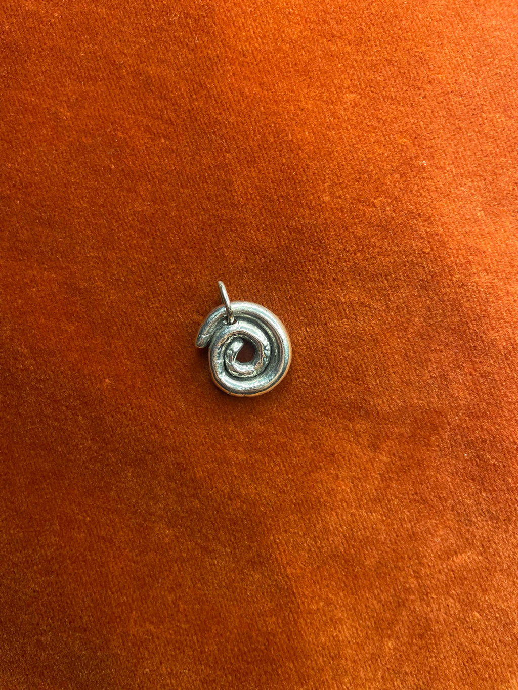 Silver spiral charm laying on an orange velvet background.