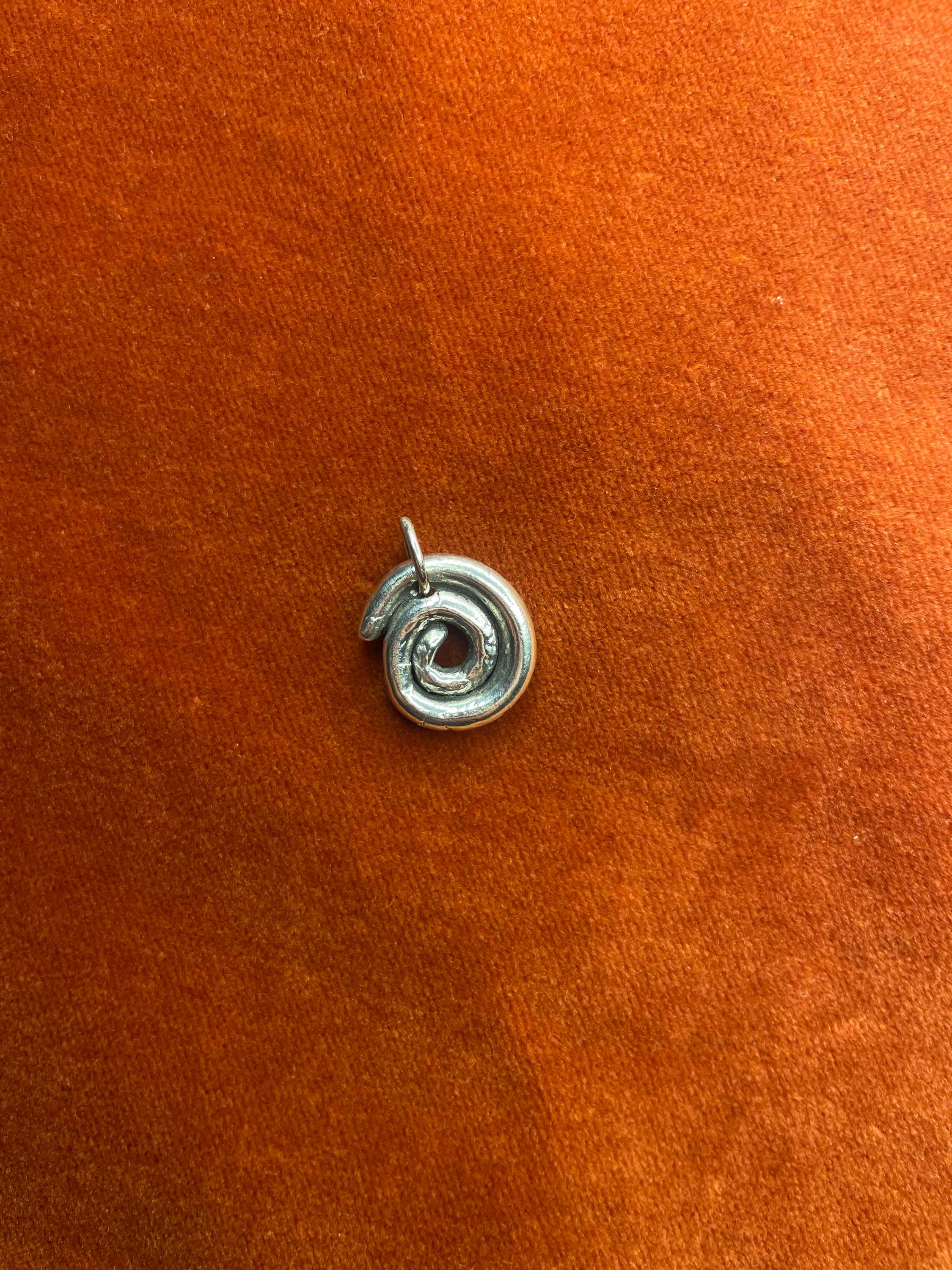 Silver spiral charm laying on an orange velvet background.