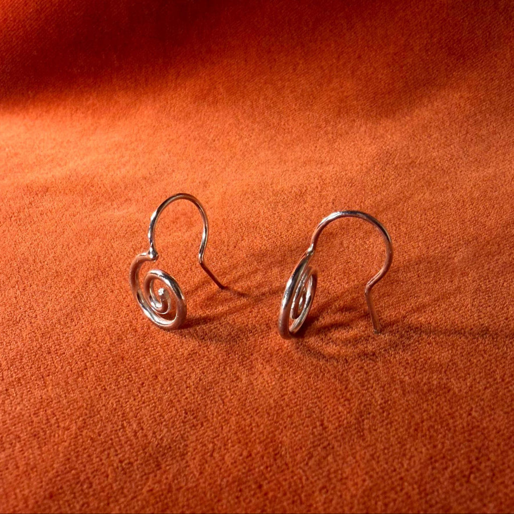 Silver earrings with a spiral design staged on an orange velvet background.