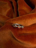 Silver ring with three small garnet stones set in a sterling silver serrated bezel on small thin band. Staged on a orange velvet background.