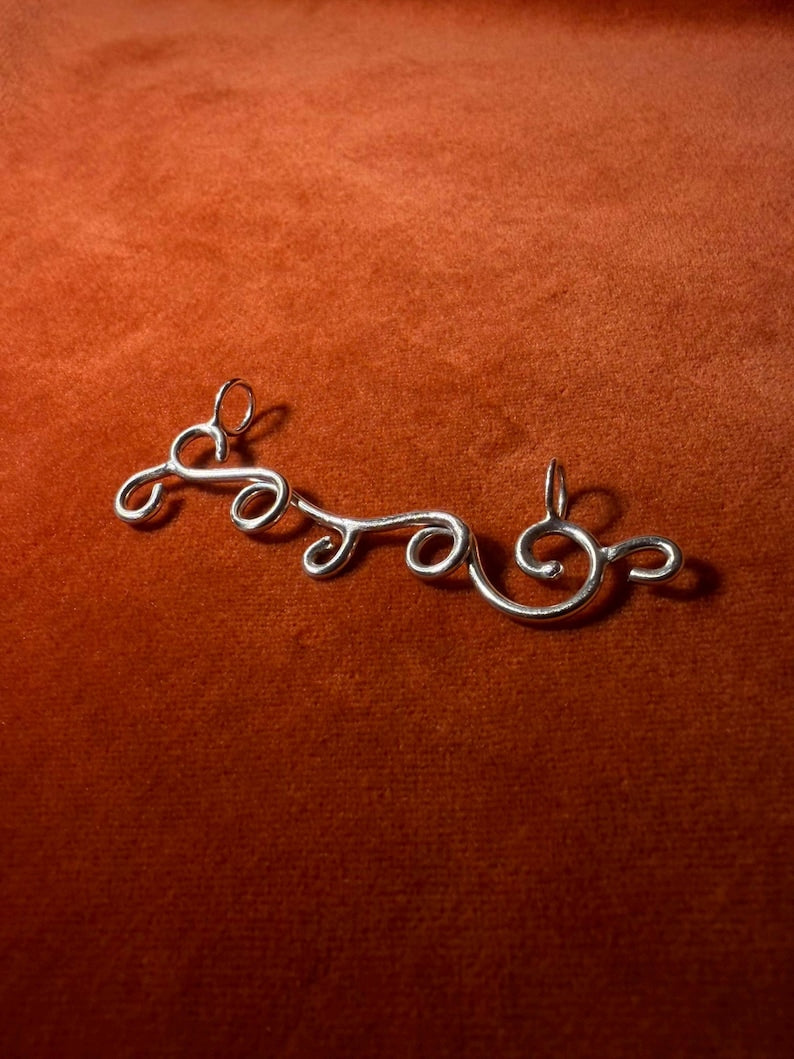 Silver charm designed in the shape of a wind swirls. Staged on an orange velvet background. 