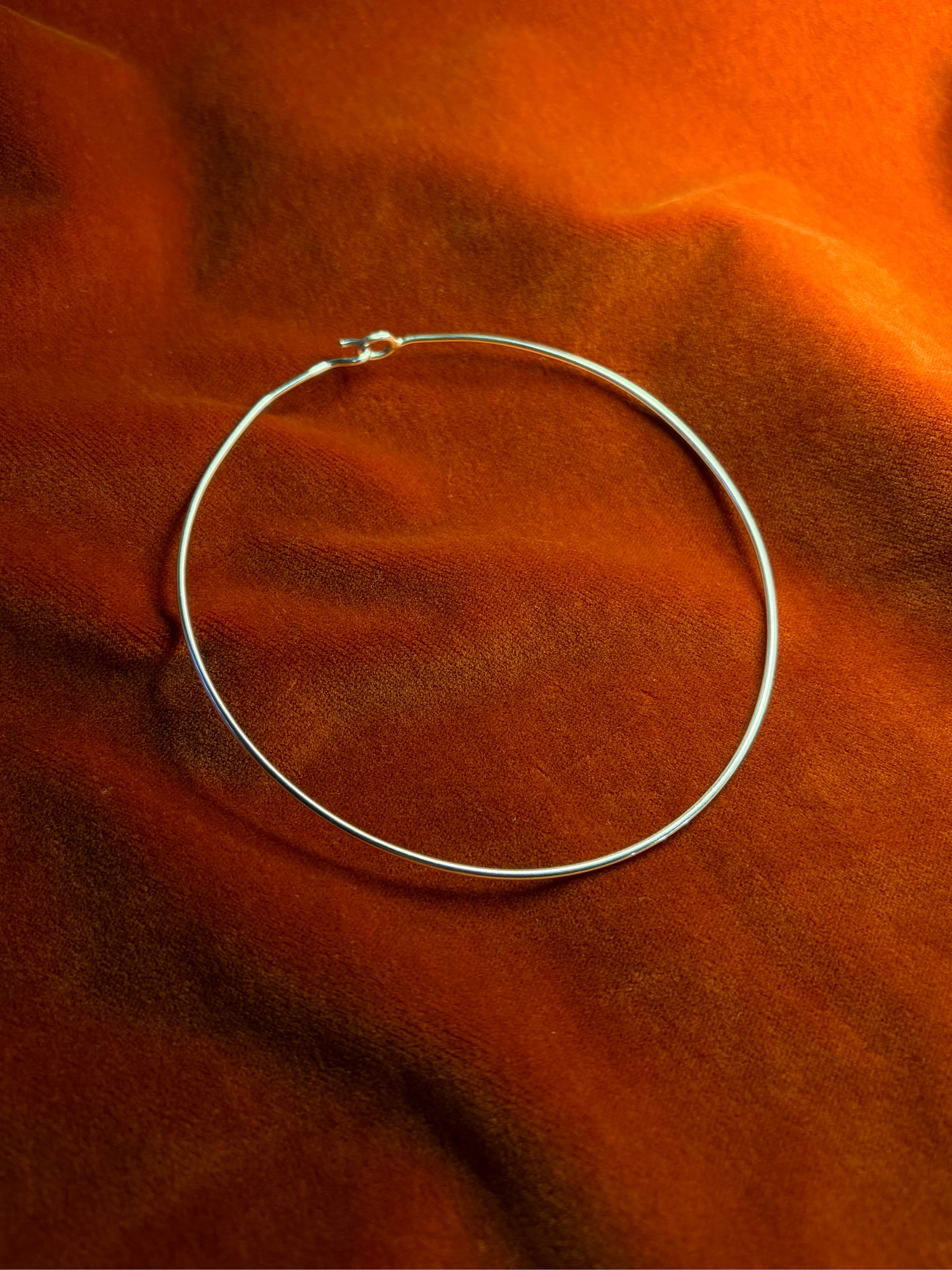 Silver wire hook choker with hook clasp. Choker is closed an and stage on a orange velvet background.
