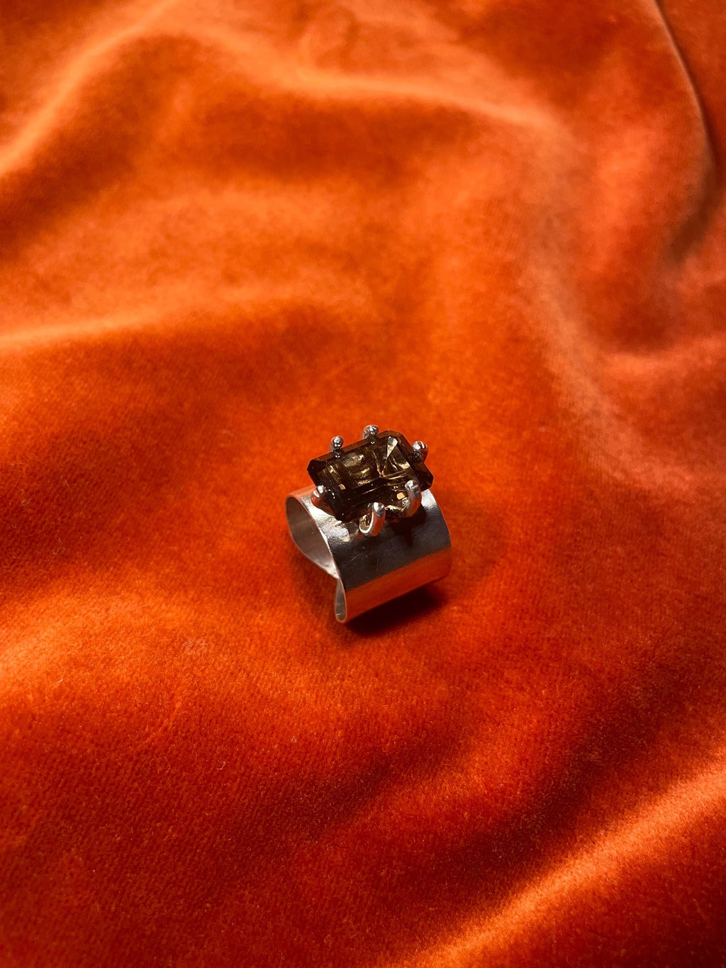 Silver ring with a smoky quartz emerald cut stone, set within five prongs on top of the large band. 