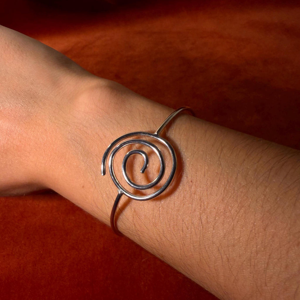 Silver bracelet with a spiral shape and a hook clasp. Pictured on a velvet backdrop.