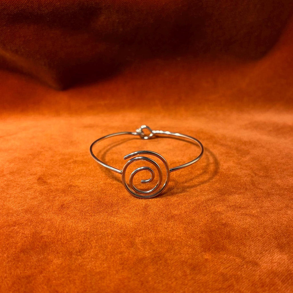 Silver bracelet with a spiral shape and a hook clasp. Pictured on a velvet backdrop.