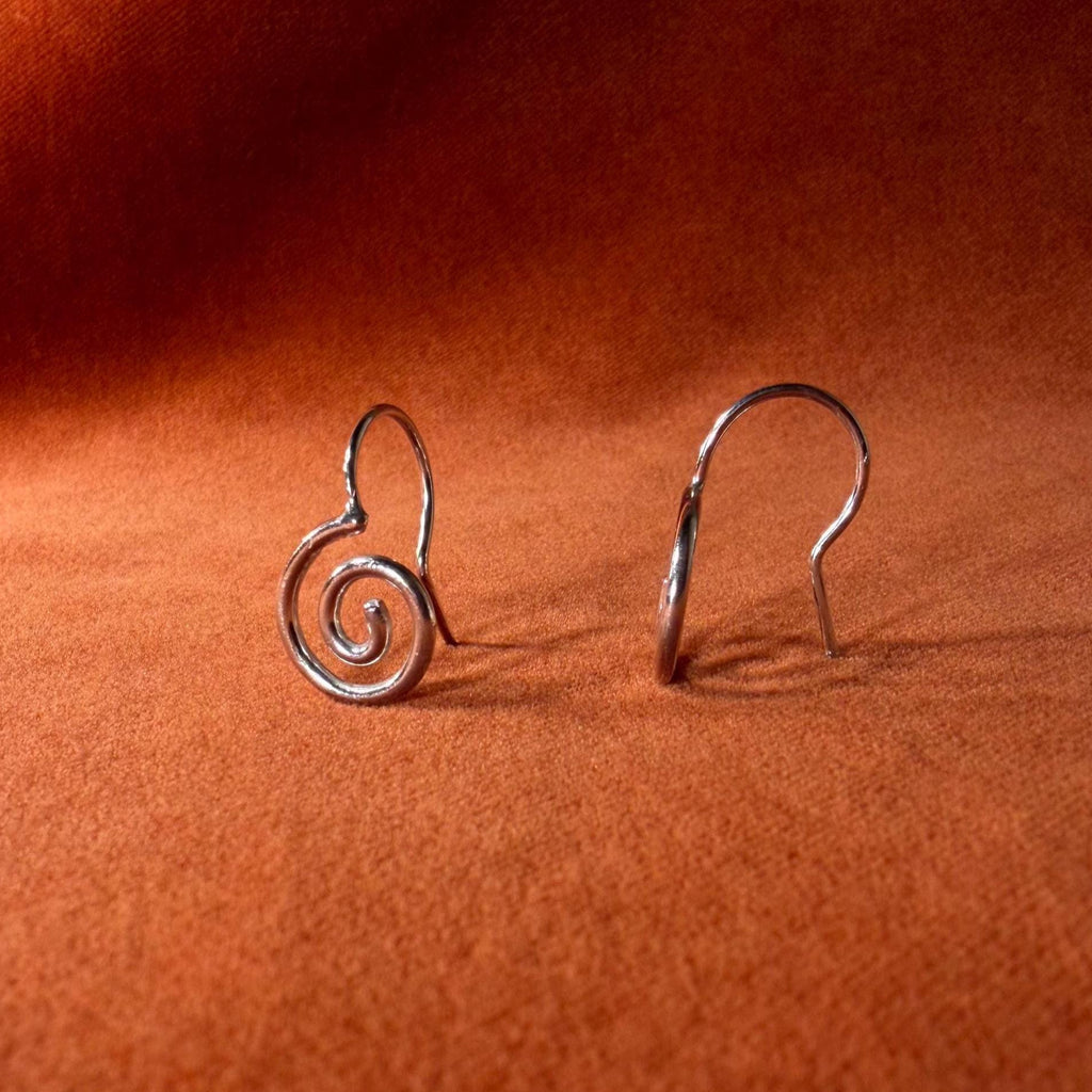 Silver earrings with a spiral design staged on an orange velvet background.