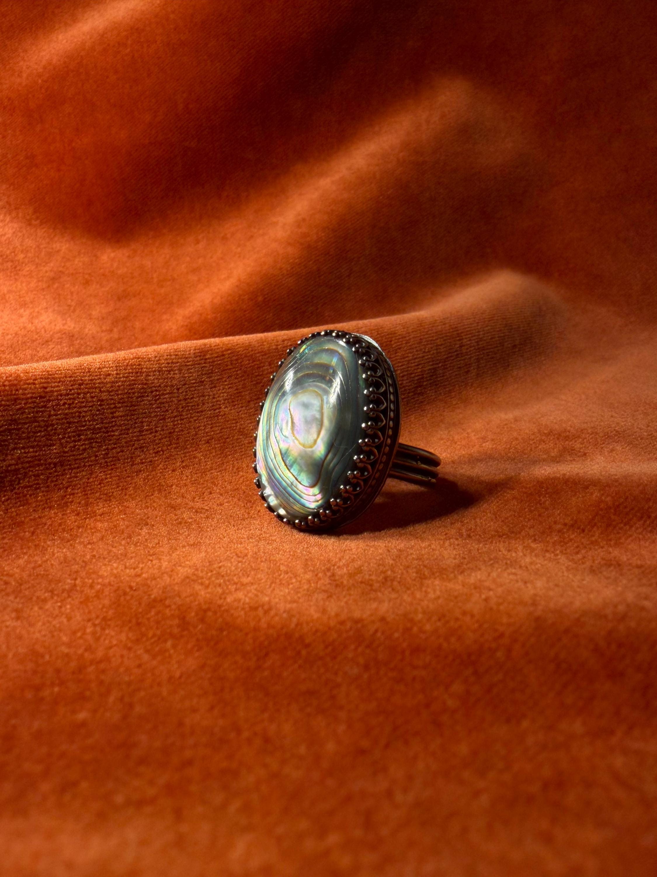 Silver ring with a colorful abalone oval shaped stone set in an ornate bezel sitting on a medium sized band.