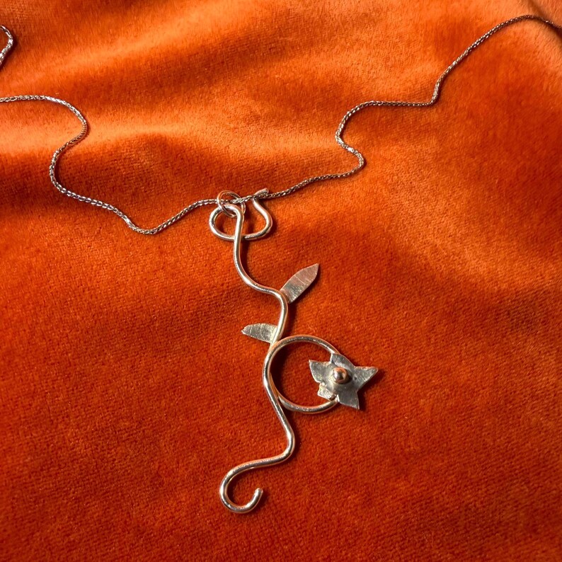 Silver jasmine flower vine charm on a silver chain laying against an orange velvet background.