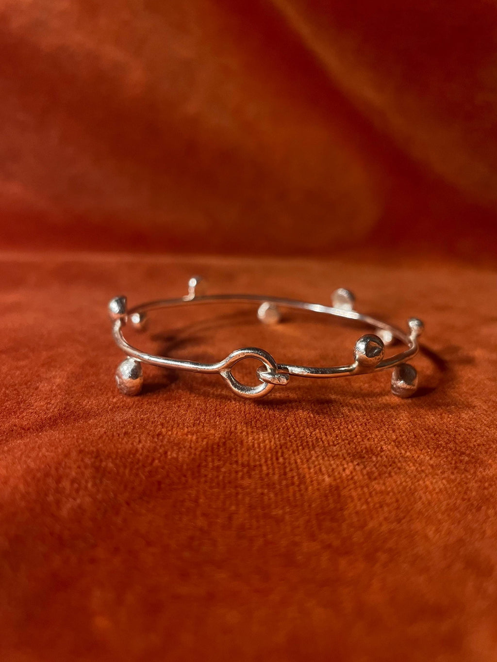 Silver bracelet showing the hook clasp closed. Ten small orbs are featured around the bracelet. Staged on an orange velvet backdrop.