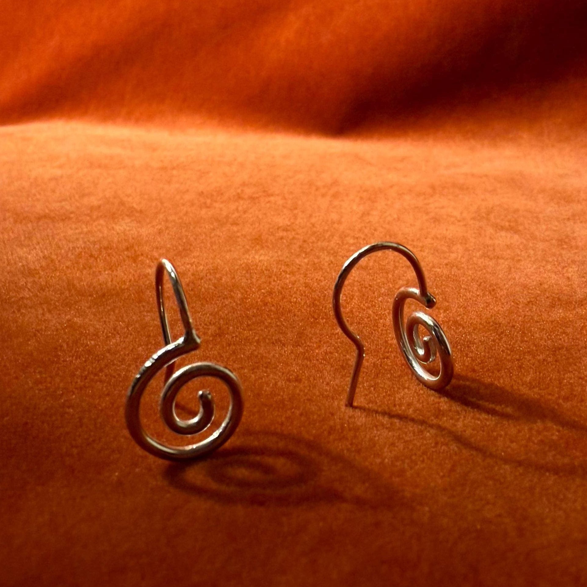 Silver earrings with a spiral design staged on an orange velvet background.
