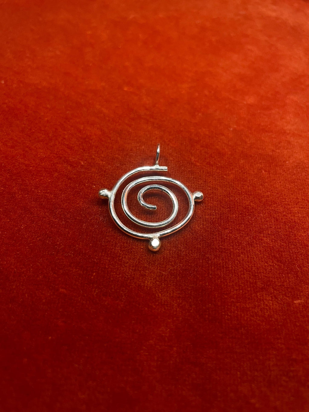 Silver spiral charm with three orbs around the edge on a red fabric background.
