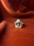 Silver ring with a flower petal design and a moss agate gemstone set in the center sitting on a small band. Staged against an orange velvet background.