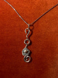 Silver chain with a silver flower vine charm laying against an orange velvet background.