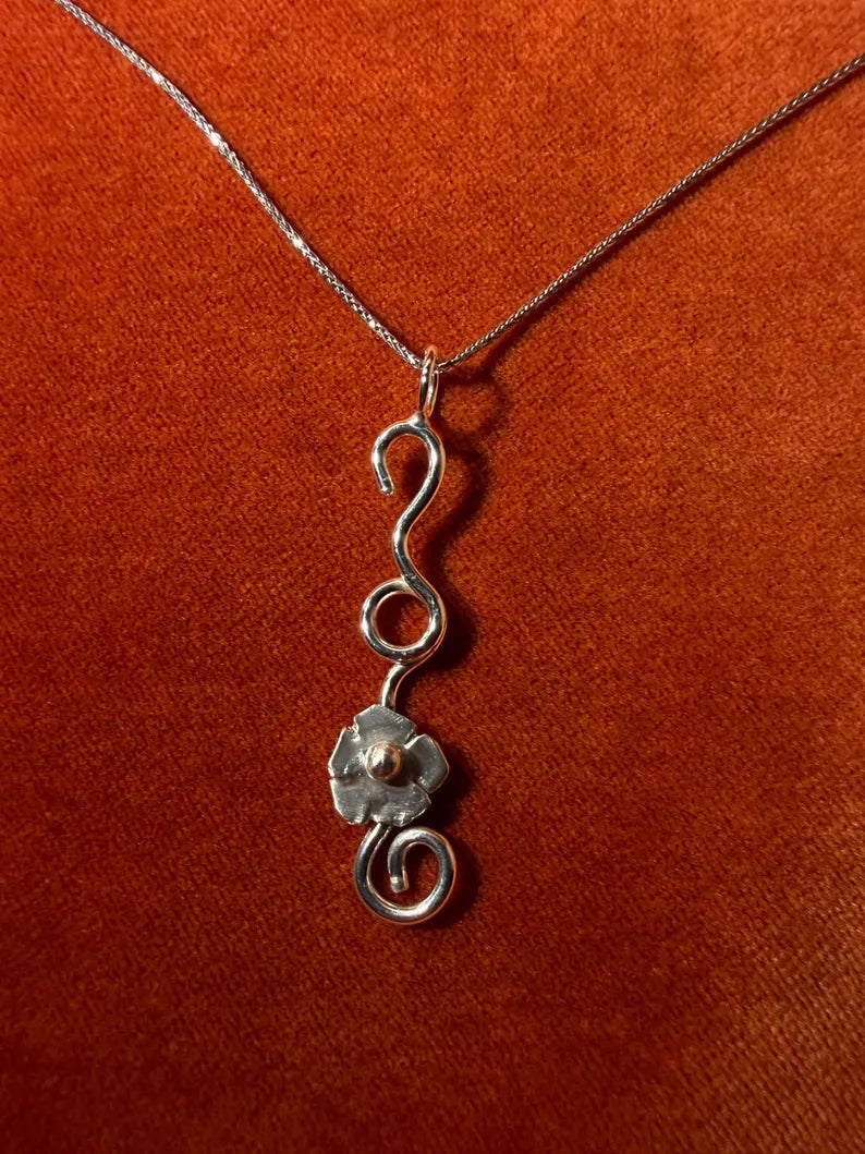 Silver chain with a silver flower vine charm laying against an orange velvet background.