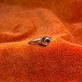 Silver ring with a serrated bezel enclosure and a rose cut garnet stone set inside sitting on a thin band. Ring is staged on an orange velvet background.