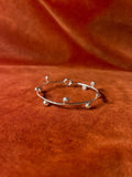 Silver bracelet with ten small orbs that wrap around circumference of the bracelet. Staged against an orange velvet background.