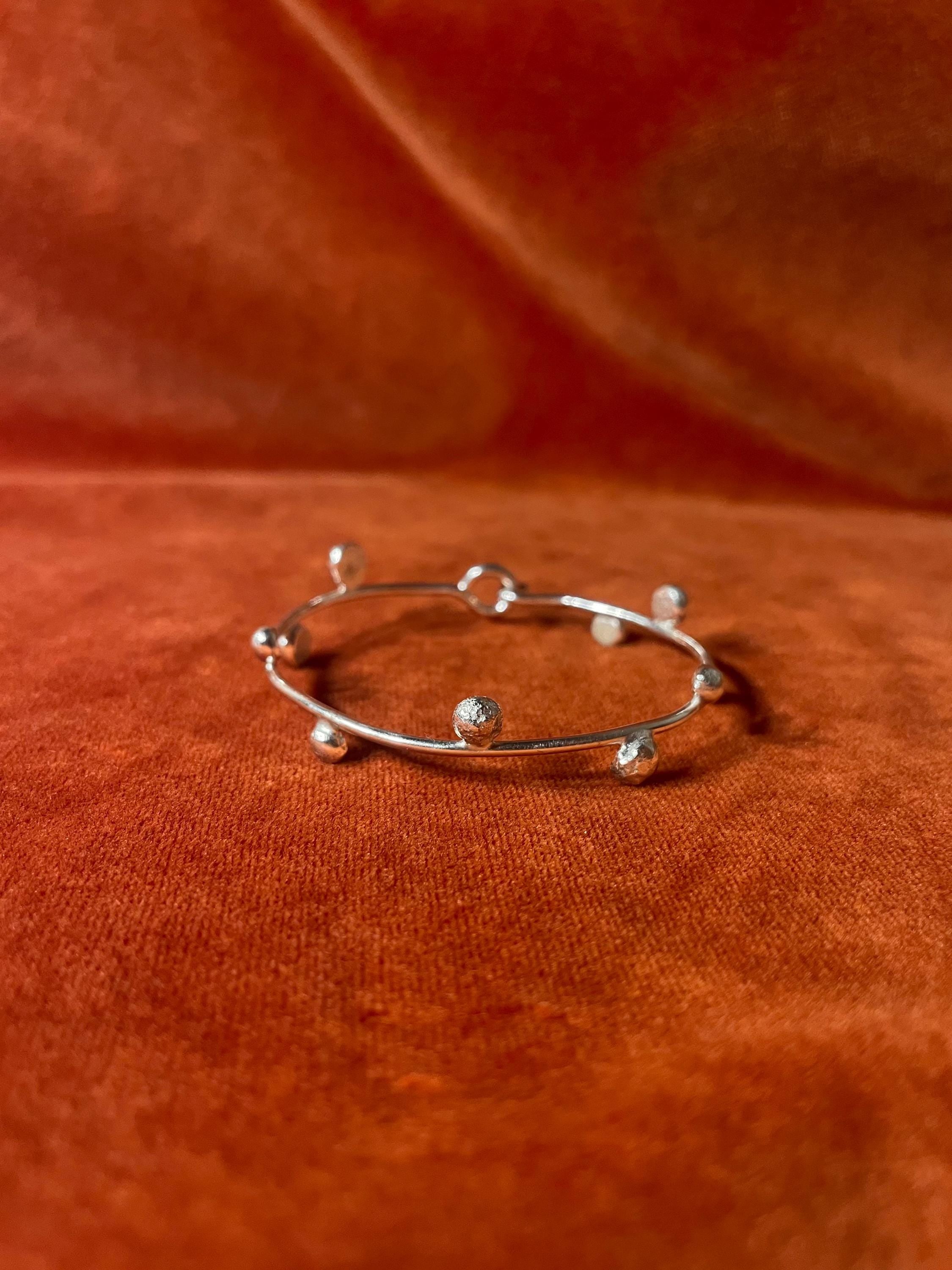 Silver bracelet with ten small orbs that wrap around circumference of the bracelet. Staged against an orange velvet background.