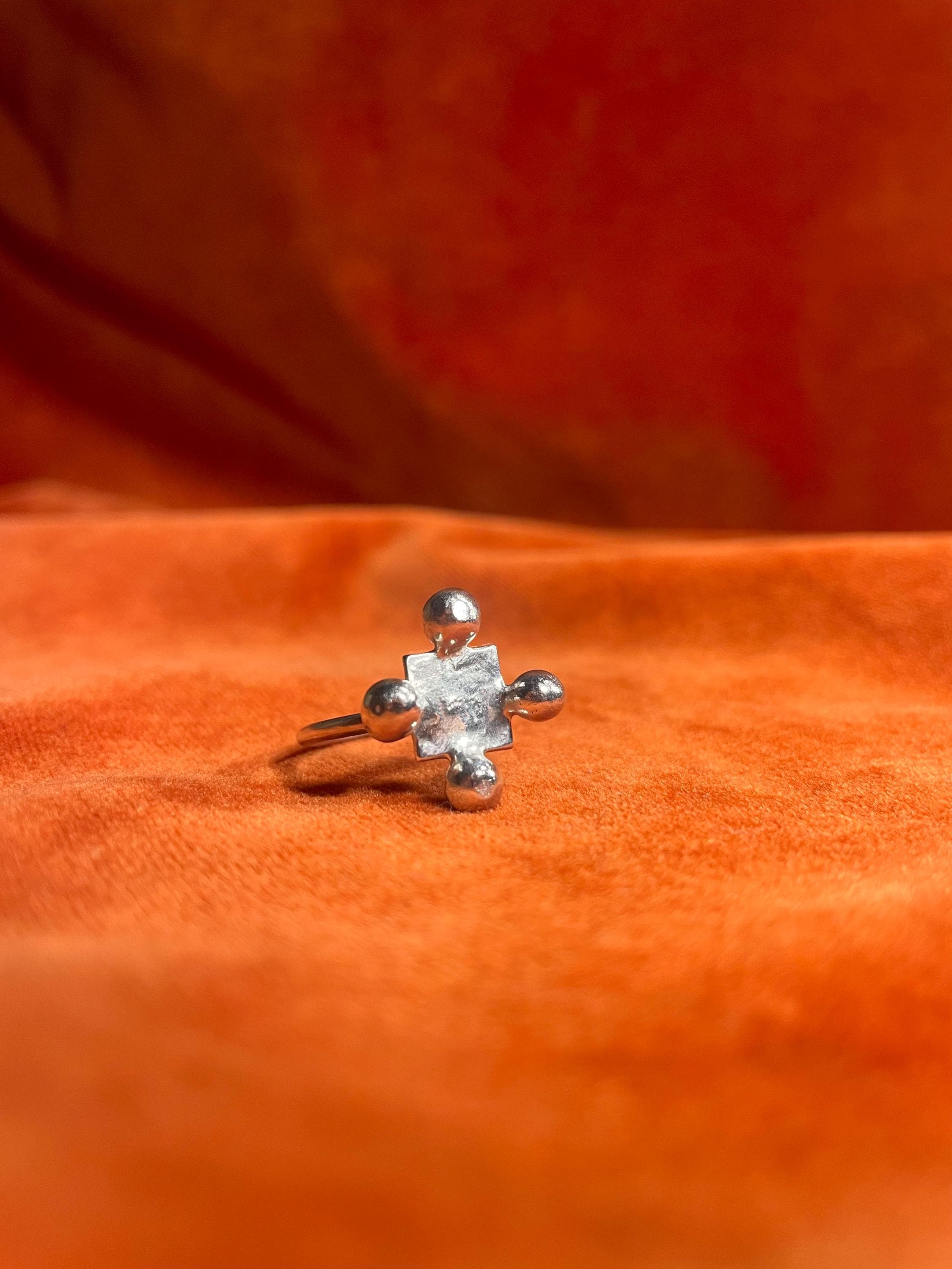Silver ring with four orbs set around a small square shape design sitting on a thin band. Staged against an orange velvet background.