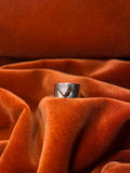 Silver ring with a pink opal stone set on a chunky band. Staged on an orange velvet backdrop.