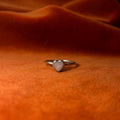 Silver ring on an orange velvet background. A pink opal heart shaped stone set in a serrated bezel sits on a thin band.