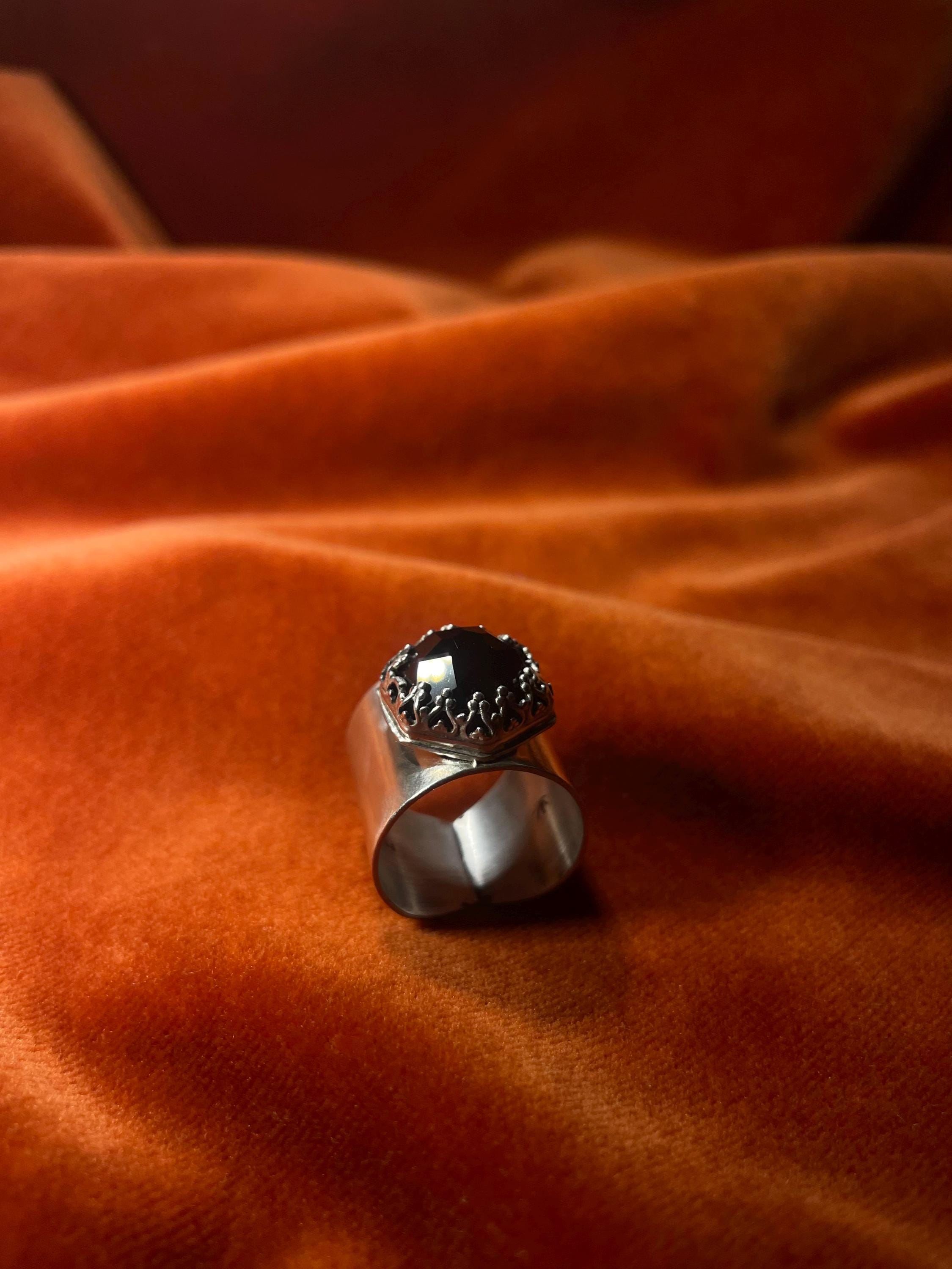 Silver ring with a black onyx rose cut stone, set on top of the large band. Ring sits against a velvet orange backdrop. 