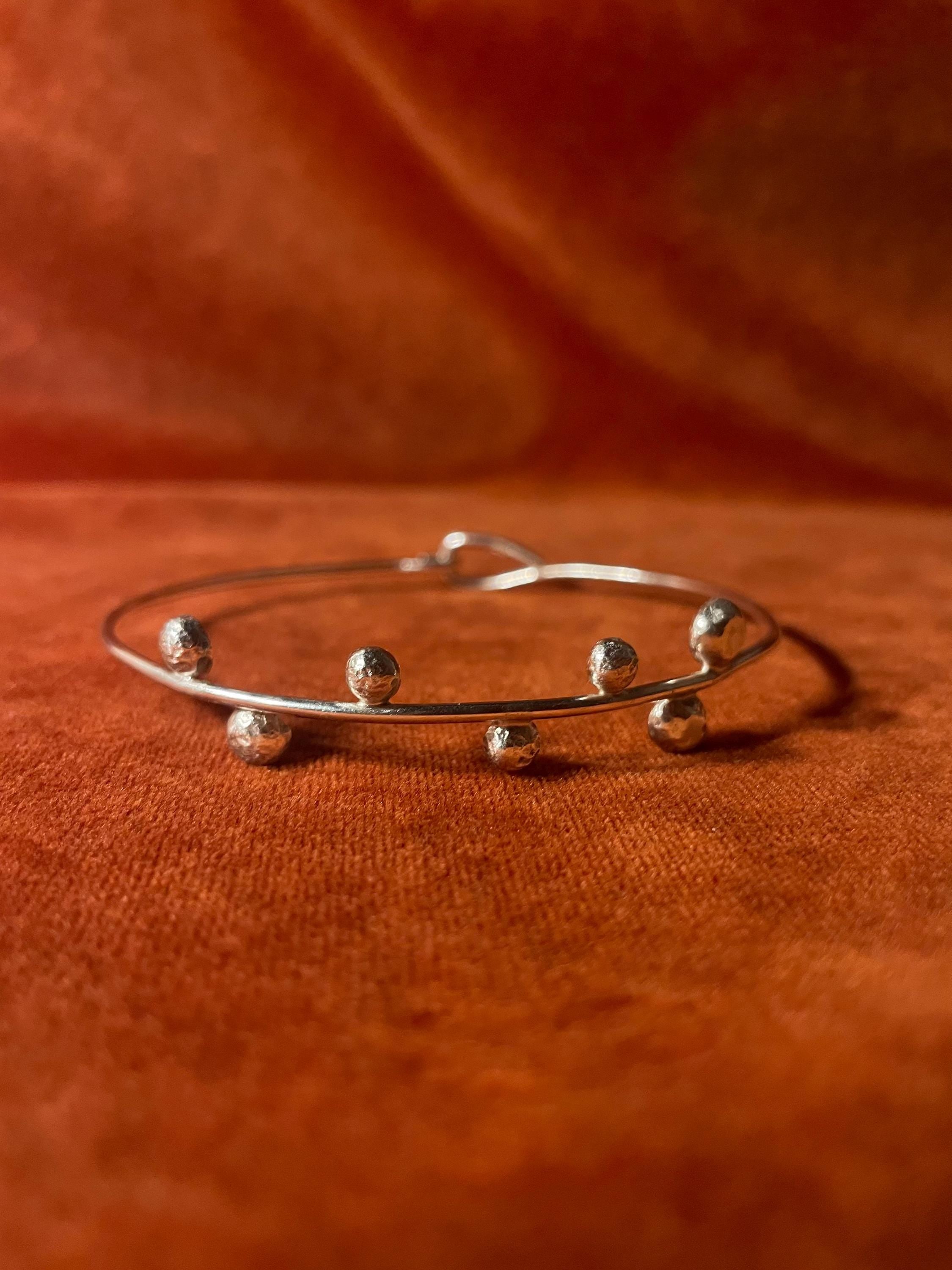 Silver bracelet with seven orbs around the bangle. Staged on an orange velvet background.