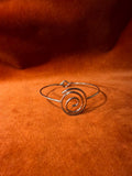 Silver bracelet with a spiral shape and a hook clasp. Pictured on a velvet backdrop.
