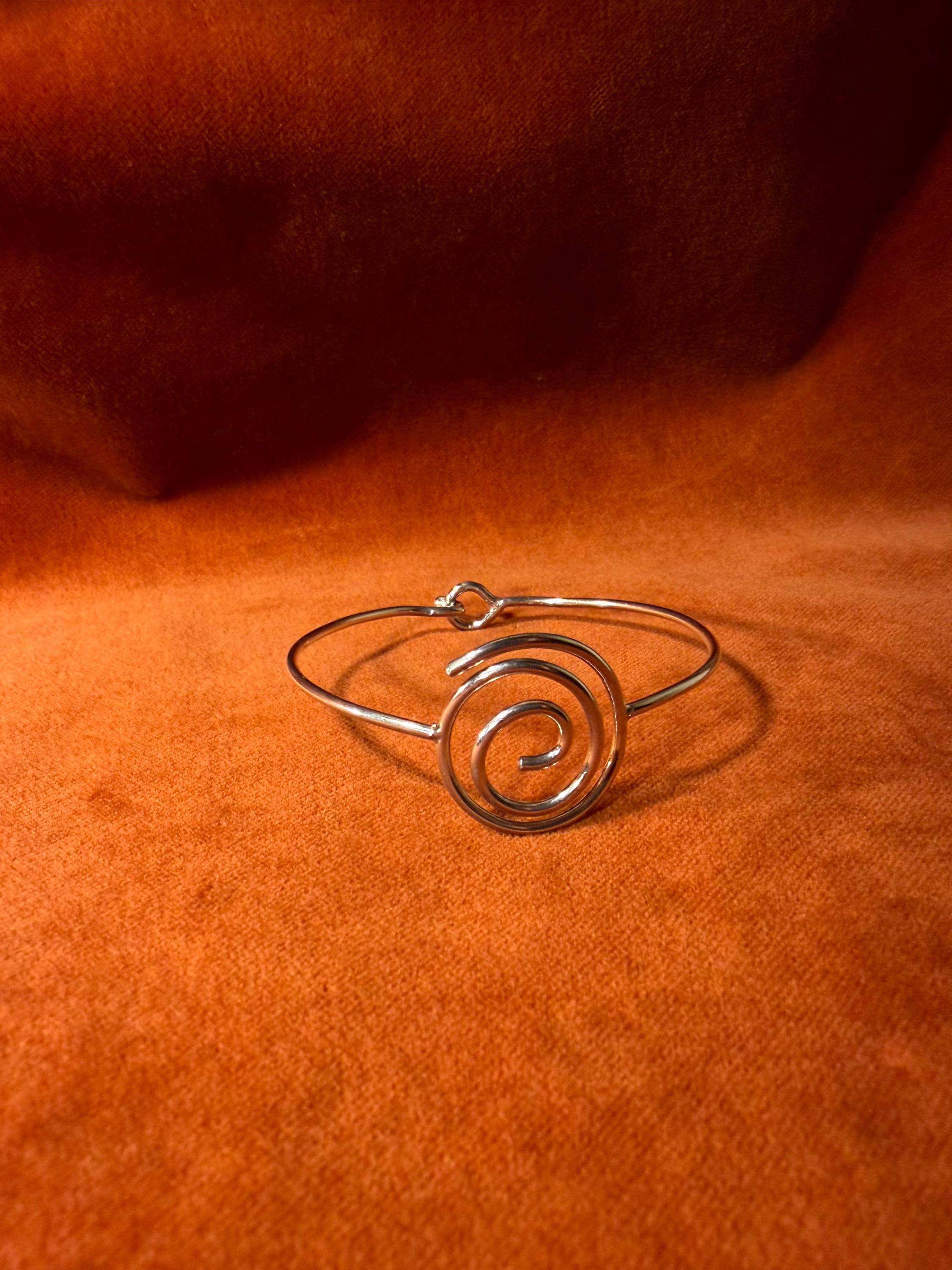 Silver bracelet with a spiral shape and a hook clasp. Pictured on a velvet backdrop.
