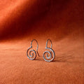 Silver earrings with a spiral design staged on an orange velvet background.
