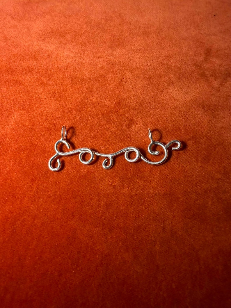Silver charm designed in the shape of a wind swirls. Staged on an orange velvet background. 