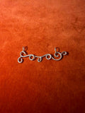 Silver charm designed in the shape of a wind swirls. Staged on an orange velvet background. 